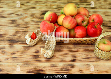 Pommes rouges et de fleurs d'automne se trouvent dans une assiette sur une table en bois. Chaussures en osier et les pommes dans un panier. L'alimentation saine et le mode de vie, le végétarisme. Banque D'Images