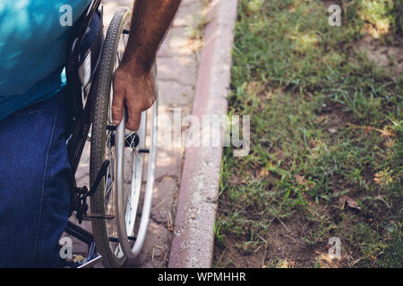 La photo en gros du jeune homme handicapé en fauteuil roulant à l'extérieur du parc en tenant Banque D'Images