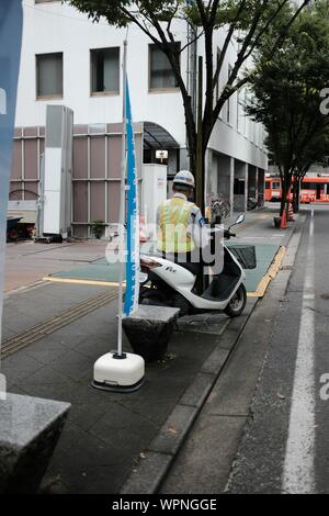 MATSUYAMA, JAPON - 20 juil 2019 : un tir vertical d'un travailleur masculin sur une moto portant un gilet et casque sur le trottoir Banque D'Images