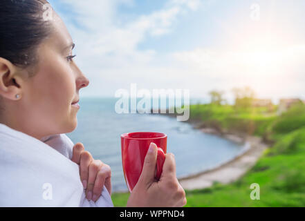 Girl enveloppé dans une couverture sur le balcon le matin boit du café ou thé. Banque D'Images