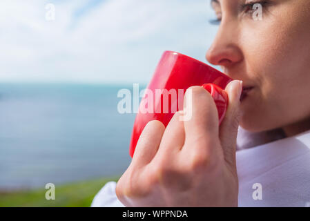 Girl enveloppé dans une couverture sur le balcon le matin boit du café ou thé. Banque D'Images