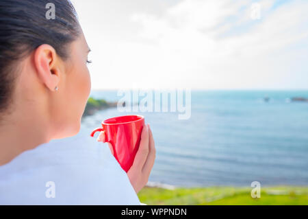 Girl enveloppé dans une couverture sur le balcon le matin boit du café ou thé. Banque D'Images