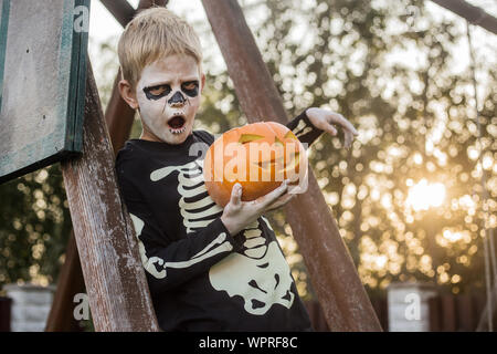 Jeune garçon aux cheveux blonds avec squelette costume holding jack o lantern. L'Halloween. Trick or Treat. Portrait en extérieur Banque D'Images