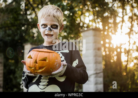 Jeune garçon aux cheveux blonds avec squelette costume holding jack o lantern. L'Halloween. Trick or Treat. Portrait en extérieur Banque D'Images