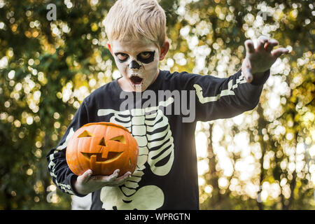 Jeune garçon aux cheveux blonds avec squelette costume holding jack o lantern. L'Halloween. Trick or Treat. Portrait en extérieur Banque D'Images