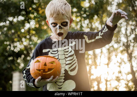 Jeune garçon aux cheveux blonds avec squelette costume holding jack o lantern. L'Halloween. Trick or Treat. Portrait en extérieur Banque D'Images