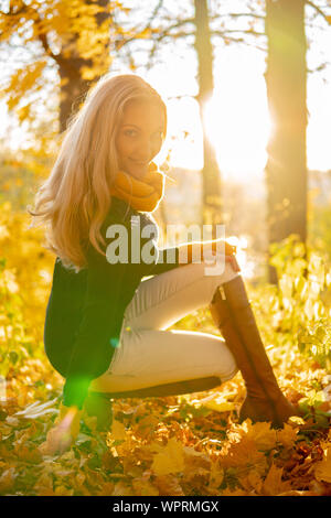 En automne, la jeune fille est assise dans la forêt, le soleil brille aux yeux du photographe. Banque D'Images