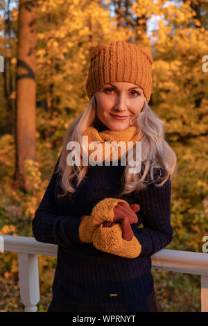 Une fille se tient sur une plate-forme blanche dans la forêt en automne en octobre, dans un chapeau, dans un chapeau, dans des mitaines, dans une veste noire Banque D'Images