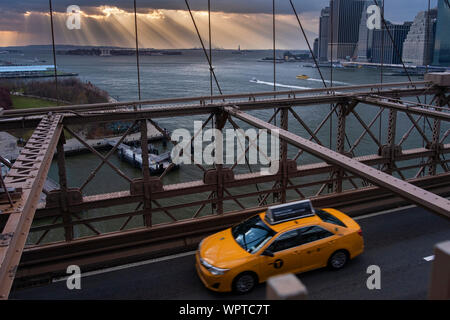 Yellow Cab, traverser le pont de Brooklyn avec les rayons du soleil sur un lointain de la Statue de la liberté, New York, USA Banque D'Images