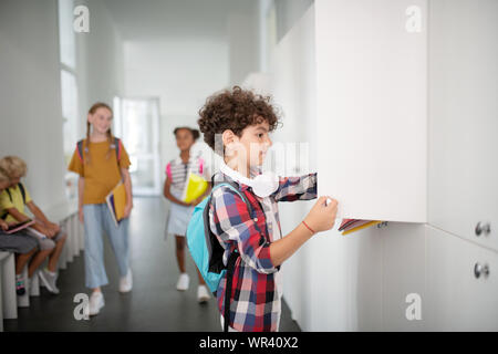 Boy wearing squared shirt casier d'ouverture tout en prenant des livres Banque D'Images