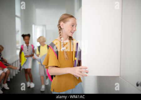 Smiling girl wearing backpack l'ouverture de son casier à l'école Banque D'Images