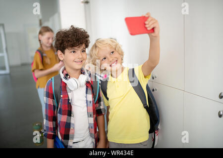 Boy holding smartphone rouge tout en faisant avec camarade selfies Banque D'Images