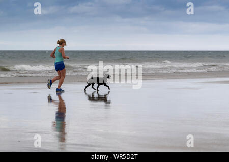 Woman jogging sur la plage de Benone avec son chien, l'Irlande du Nord, Royaume-Uni. Banque D'Images