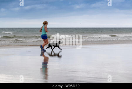 Woman jogging sur la plage de Benone avec son chien, l'Irlande du Nord, Royaume-Uni. Banque D'Images