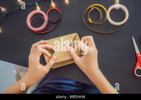 Jeune femme est présente d'emballage. Présent enveloppé dans du papier craft avec un ruban rouge et or pour Noël, anniversaire, fête des mères ou la saint valentin Banque D'Images