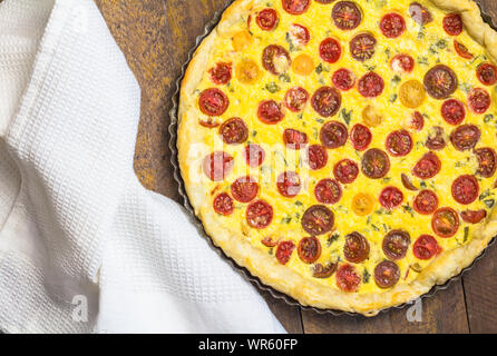 Quiche aux tomates cerises avec œuf et fromage remplissant un moule avec torchon sur table en bois - haut voir photo Banque D'Images