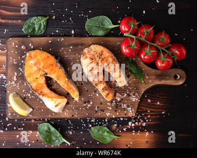 Vue de dessus du saumon sur un fond en bois et avec un peu d'épinards feuilles autour. Le sel et le poivre avec des tomates Banque D'Images