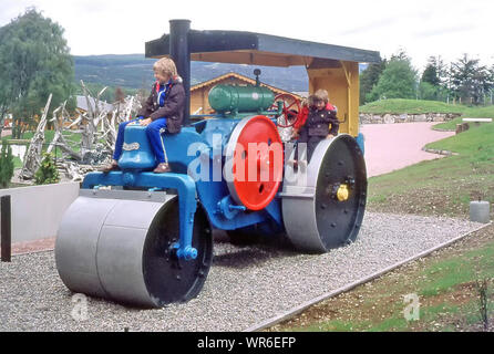 Archives historiques des années 1970 famille en voyage de vacances rouleau de vapeur coloré dedans Aire de jeux pour enfants, deux garçons et une maman avec une fille à l'arrière Comment nous étions dans les années 70 Aviemore Scottish Highlands Royaume-Uni Banque D'Images