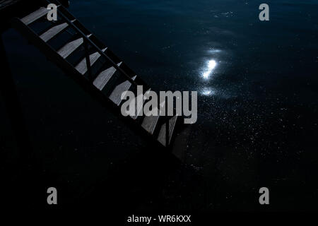 Un escalier descendant dans l'eau de nuit comme le clair de lune se reflète sur la surface des eaux Banque D'Images