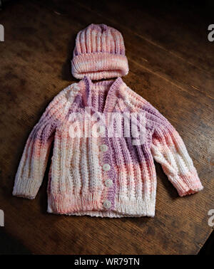 Côté tricoté par Carole un cardigan bébé et chapeau, créé à partir de fil acrylique dans des tons de mauve, rose et blanc. Banque D'Images