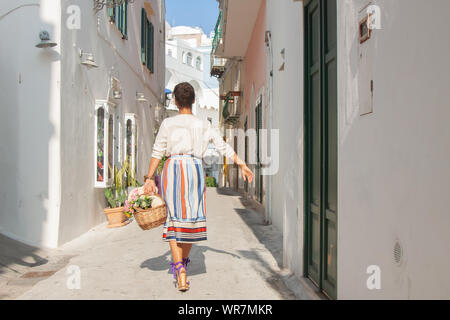 Jeune femme marchant dans une ruelle typique sur l'île de Ponza, ville de l'Italie. Robe a la mode et lunettes, bâtiment blanc. Banque D'Images