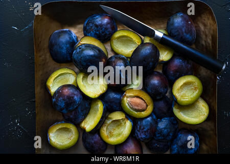 Vue du haut vers le bas de tranches de prunes bleu et le couteau sur un plateau de métal, orientation horizontale vue rapprochée Banque D'Images