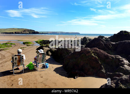 Un couple de profiter du soleil, assis sur la plage à Bigbury-on-Sea, dans le sud du Devon où il y a un accès à l'île de Burgh Hôtel et le pilchard d'Inn. Banque D'Images