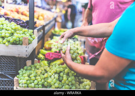 Close up of hands holding grapes à street market avec divers fruits et légumes colorés en arrière-plan. Banque D'Images