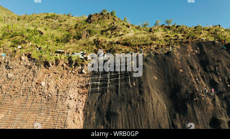 Renforcer les travailleurs la pente de la montagne avec le grillage de métal prévenir les chutes de pierres et glissements de terrain sur la route, vue ci-dessus. Les travailleurs de la construction de mur de béton anti-glissement prévenir protéger contre les glissements rocheux concept de sécurité. Banque D'Images