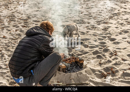 Man cooking barbecue sur la plage. Pique-nique sur la plage fluviale avec husky puppy. Banque D'Images