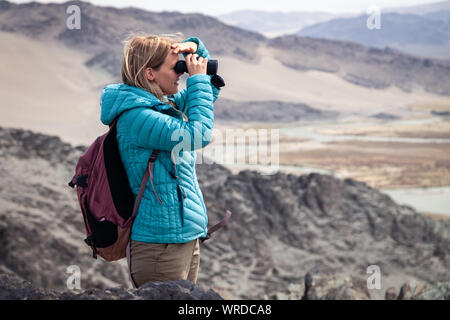 La Mongolie Ulgii 2019-05-04 European belle fille de veste bleue à la binoculaire par dans la distance, l'observation de l'aigle, randonnées, escalade, walkin Banque D'Images