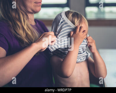 Une jeune mère aide son petit bambin mis sur une chemise Banque D'Images