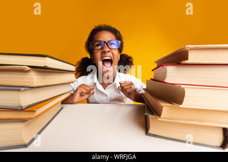 Petite fille en colère crier font leurs devoirs assis entre les piles de livres Banque D'Images