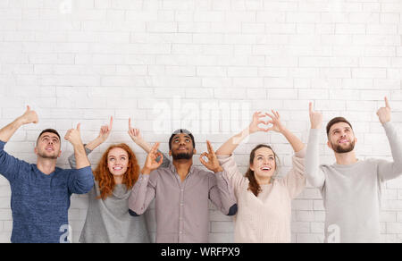 Jeunes amis montrant différents gestes sur mur blanc Banque D'Images