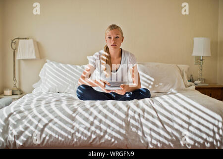 Jeune femme assise dans sa chambre à coucher soleil recherche dans l'anxiété et préoccupation choqué après avoir lu quelque chose sur sa tablette électronique. Banque D'Images