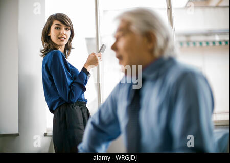 Young businesswoman en utilisant un téléphone intelligent comme son patron travaille dans une réunion. Banque D'Images