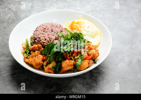 Poulet croustillant cuit avec le basilic vert, servi avec du riz vapeur et œuf frit, chaud et plat épicé avec des feuilles de basilic. Banque D'Images