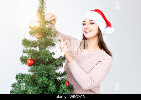 Jours fériés et des fêtes concept - Happy brunette woman in Santa's hat décore un arbre de Noël à la maison dans le salon. Banque D'Images