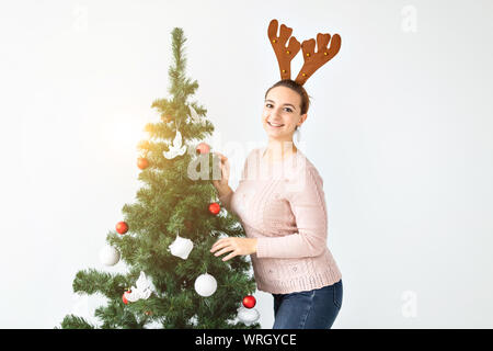 Jours fériés et des fêtes concept - Happy brunette woman dans drôle deer hat décore un arbre de Noël à la maison dans le salon. Banque D'Images