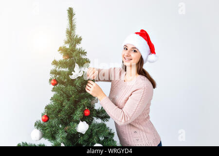 Jours fériés et des fêtes concept - Happy brunette woman in Santa's hat décore un arbre de Noël à la maison dans le salon. Banque D'Images