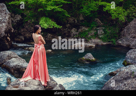 Sorcière de la rivière, assis sur un rocher dans la rivière. Robe rose, une image à la mode fabuleux.tonifiant. Couleur créative. Belle danseuse dans une forêt mystique b Banque D'Images