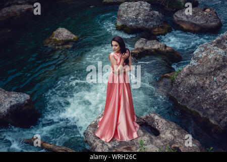 Sorcière de la rivière, assis sur un rocher dans la rivière. Robe rose, une image à la mode fabuleux.tonifiant. Couleur créative. Belle danseuse dans une forêt mystique b Banque D'Images