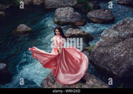 Sorcière de la rivière, assis sur un rocher dans la rivière. Robe rose, une image à la mode fabuleux.tonifiant. Couleur créative. Belle danseuse dans une forêt mystique b Banque D'Images