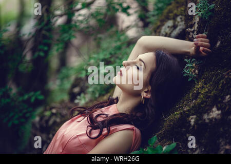 Sorcière de la rivière, assis sur un rocher dans la rivière. Robe rose, une image à la mode fabuleux.tonifiant. Couleur créative. Belle danseuse dans une forêt mystique b Banque D'Images