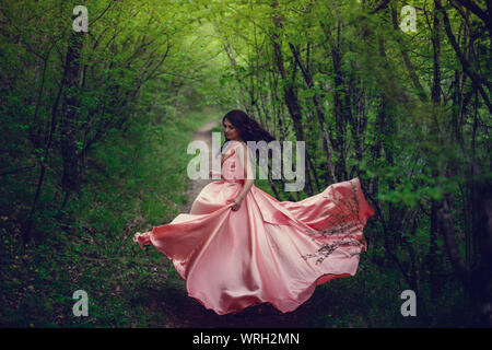 Sorcière de la rivière, assis sur un rocher dans la rivière. Robe rose, une image à la mode fabuleux.tonifiant. Couleur créative. Belle danseuse dans une forêt mystique b Banque D'Images