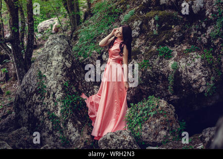 Sorcière de la rivière, assis sur un rocher dans la rivière. Robe rose, une image à la mode fabuleux.tonifiant. Couleur créative. Belle danseuse dans une forêt mystique b Banque D'Images