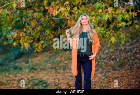 Adorable petite fille blonde posing in outfit chaleureux et cosy de l'automne nature fond flou. Création pour agréable fin de semaine. Femme à pied. La lumière au coucher du soleil Tenues décontractées confortable pour la fin de l'automne. Tenue confortable. Banque D'Images