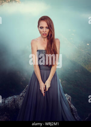 Portrait d'été dehors belle furieux guerrier scandinave ginger femme en robe grise avec métal chaîne mail. Haut dans la montagne, brouillard et mon Banque D'Images