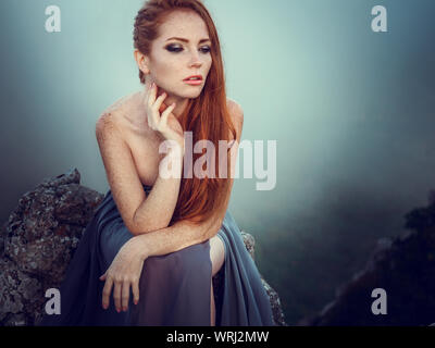 Portrait d'été dehors belle furieux guerrier scandinave ginger femme en robe grise avec métal chaîne mail. Haut dans la montagne, brouillard et mon Banque D'Images