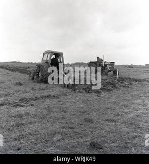 Années 1960, historique, un concours de labour, deux agriculteurs sur les tracteurs, l'un dans la cabine du tracteur, l'autre couverte d'un tracteur laboure un champ, England, UK. Les points sont attribués pour la linéarité et la propreté des sillons. Banque D'Images